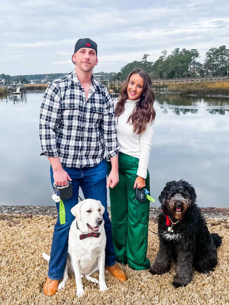 Man and woman standing on grass beside a lake with two dogs, capturing the friendly, active lifestyle associated with NJB Training in Mount Pleasant, SC.